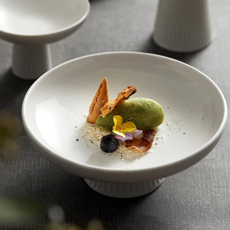 A tall, round ceramic fruit bowl in white